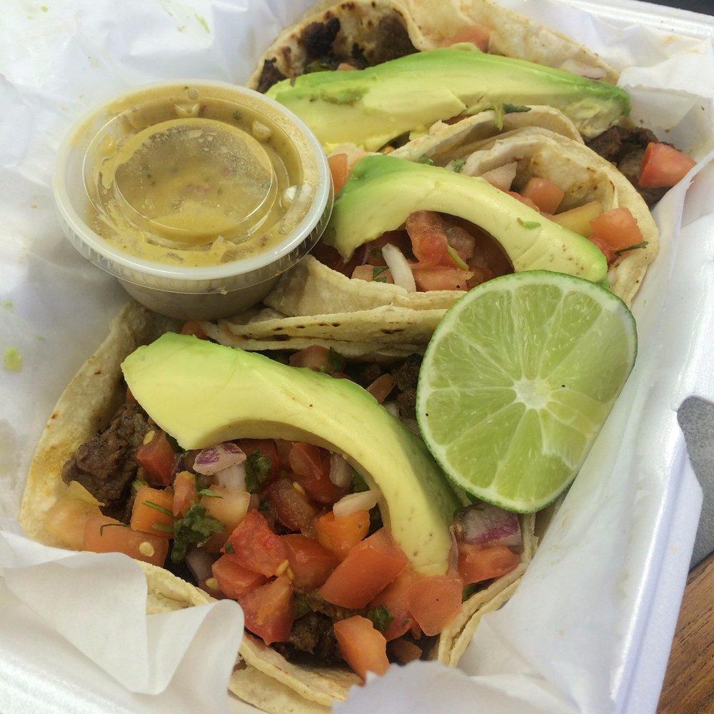 Three steak tacos with avocado and lime, packed for takeout